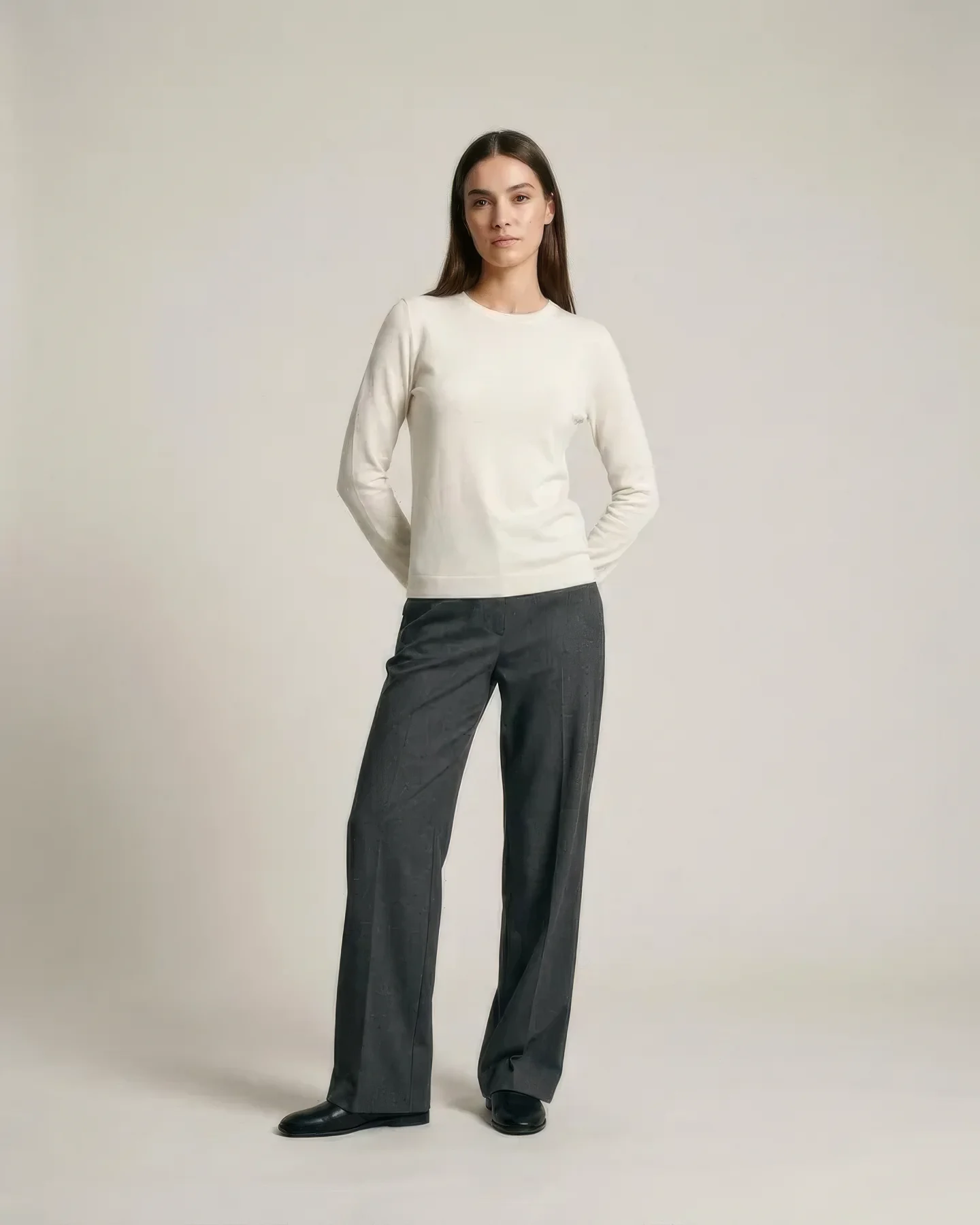 A model in a cream knit and grey wide-leg trousers, three-quarter stance